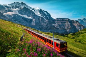 Fantastic cogwheel railway with electric red tourist train. Snowy Jungfrau mountains with glaciers, flowery fields and red passenger train, Kleine Scheidegg, Grindelwald, Bernese Oberland, Switzerland, Europe