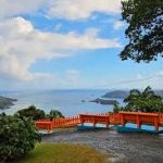 Pink sand beach with turquoise waves and rugged cliffs under a bright blue sky.